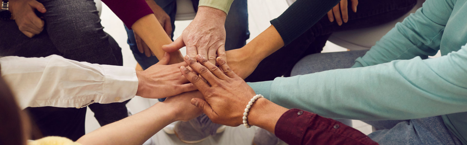 different ages and nationalities fold their hands on each other, symbolizing their unity and support